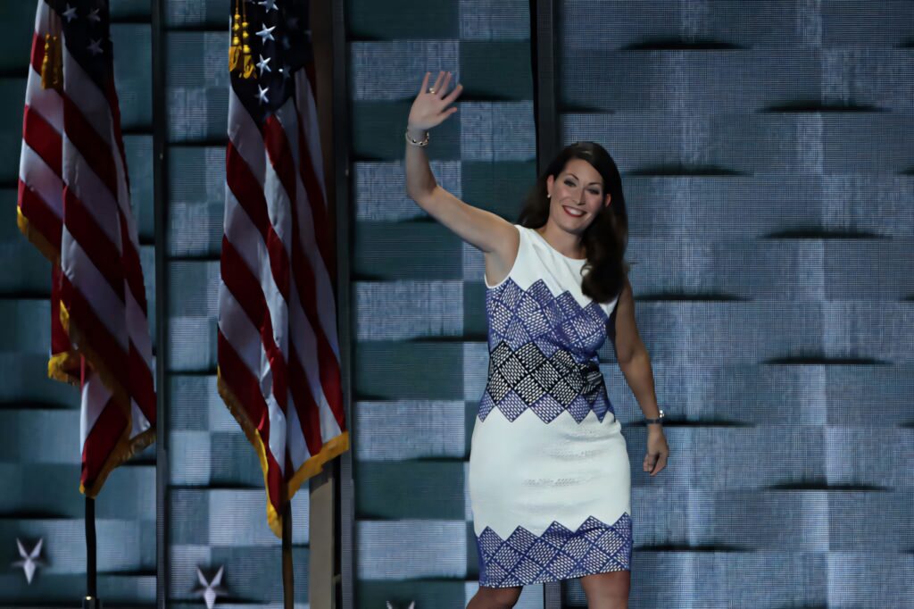 Alison Lundergan Grimes smiling and waving on stage with American flags as backdrop wallpaper
