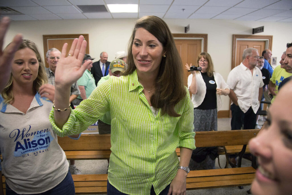 Alison Lundergan Grimes smiling and engaging with supporters at oath-taking event in casual setting Wallpaper