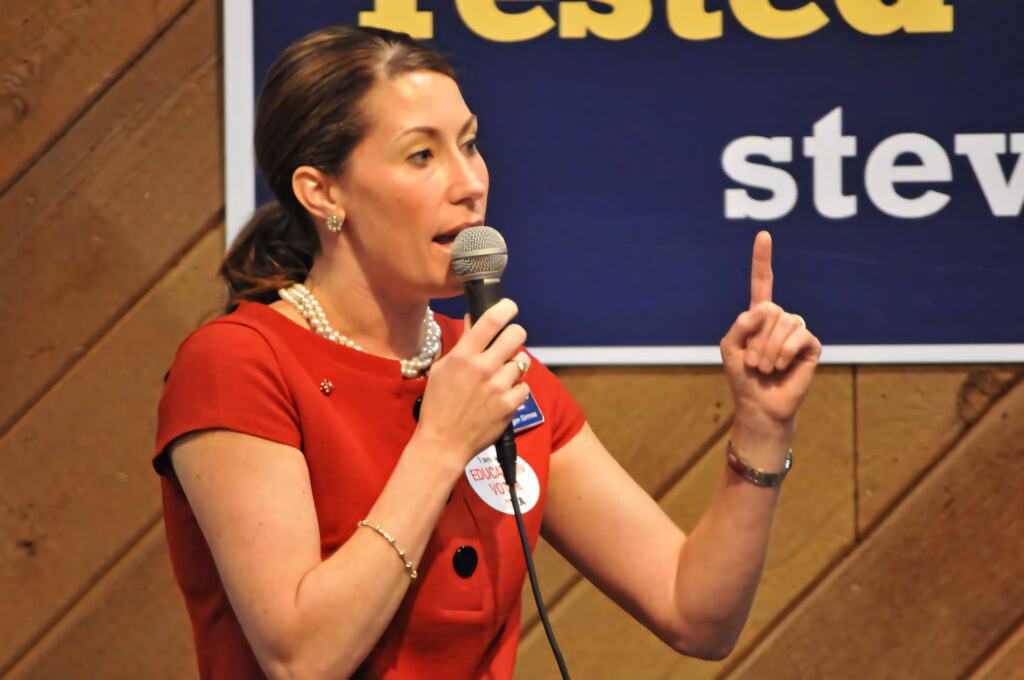 Alison Lundergan Grimes speaking confidently with hand gesture against wallpaper background