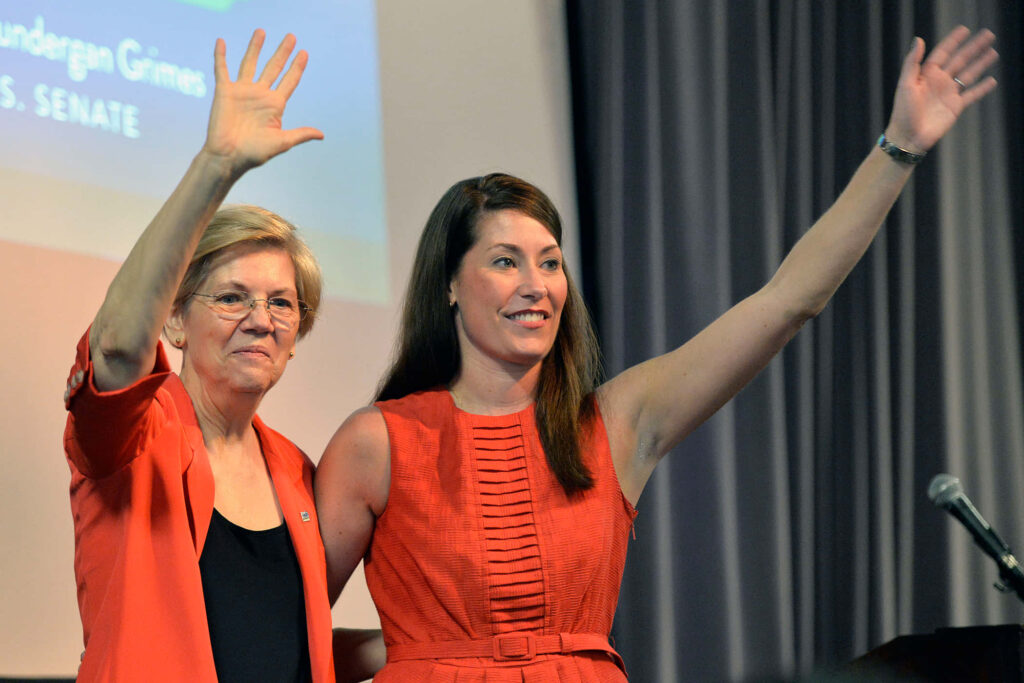 Alison Lundergan Grimes and Elizabeth Warren smiling waving in vibrant red outfits on stage Wallpaper