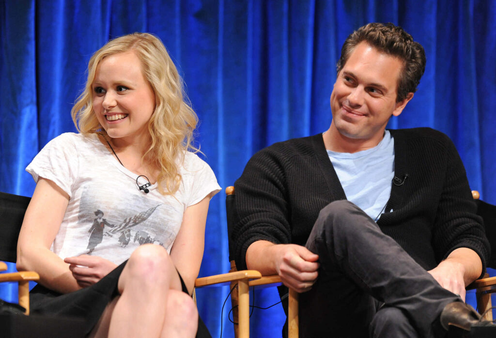 Alison Pill smiling warmly next to companion at event in casual white and black outfit wallpaper background