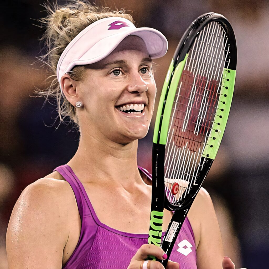 Alison Riske-Amritraj smiling on tennis court in purple tank top and white visor holding racket Wallpaper