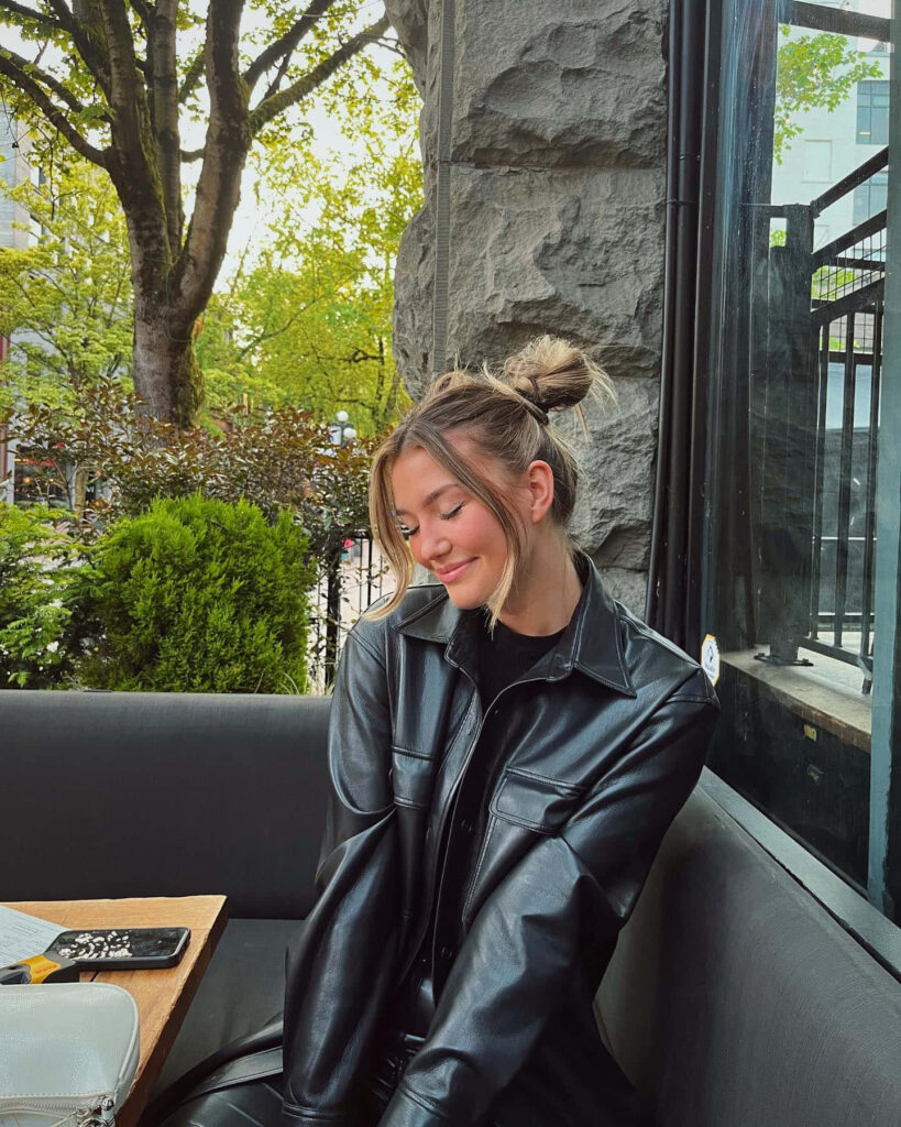 Alissa Skovbye smiling outdoors in a leather jacket surrounded by greenery and natural light Wallpaper