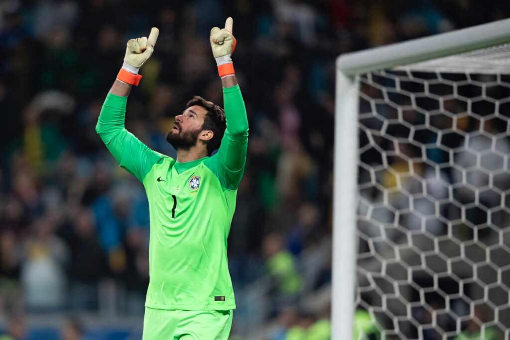 Alisson Becker in bright green Brazil goalkeeper kit celebrating by goal with fingers pointed up Wallpaper