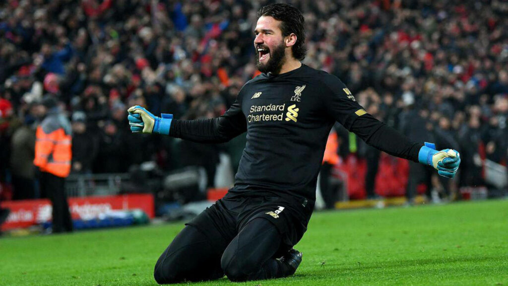 Alisson Becker celebrating passionately in Liverpool kit on field with vibrant crowd behind Wallpaper