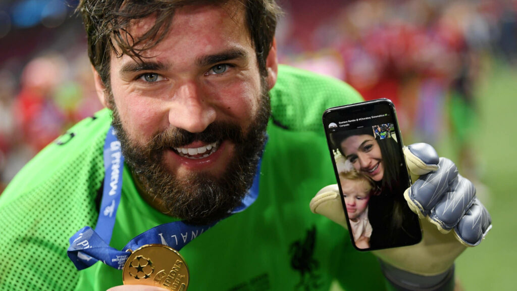 Alisson Becker celebrates football victory Facetime call with wife child showing winner medal Wallpaper
