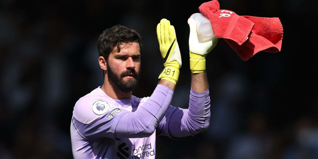 Alisson Becker clapping in goalkeeper kit holding water bottle and red towel on football field wallpaper
