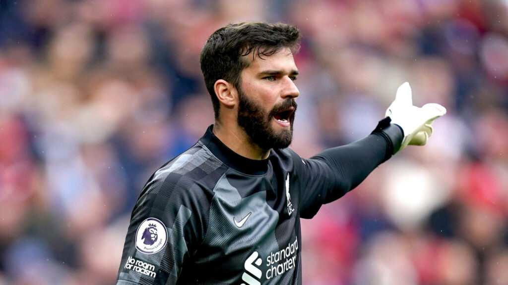 Alisson Becker in goalkeeper kit pointing and directing teammates during intense football match Wallpaper