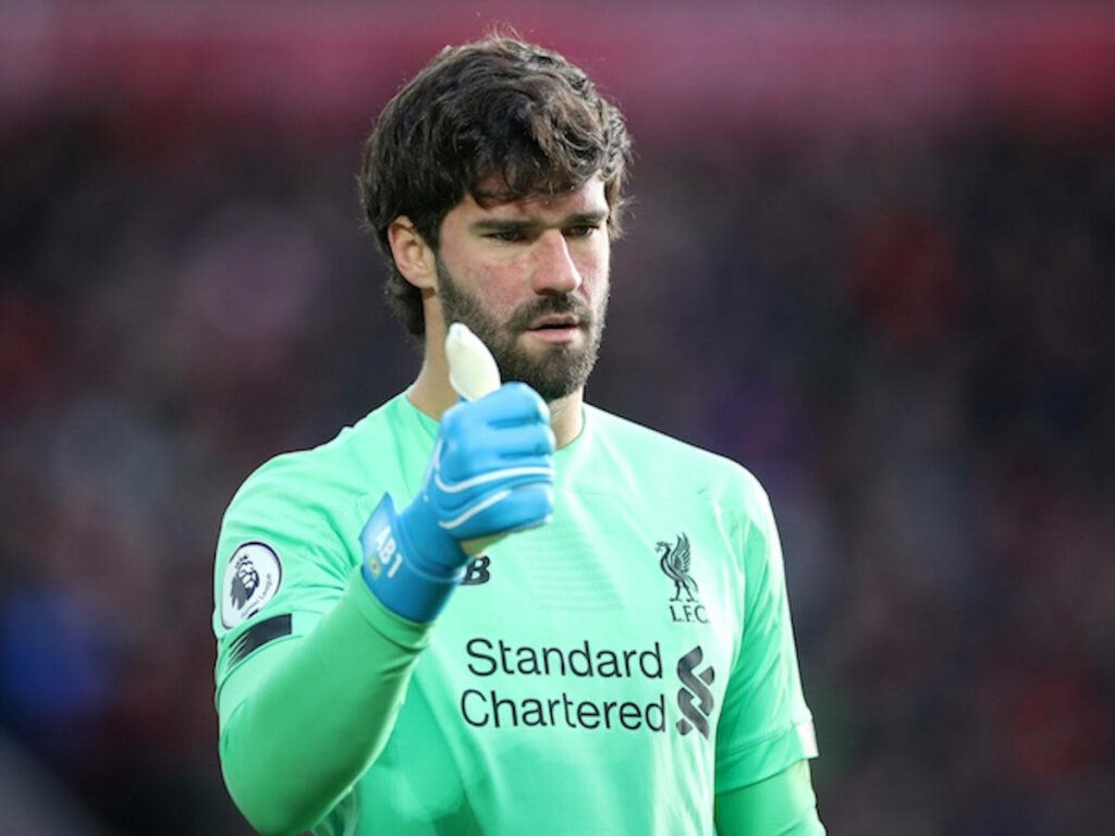 Alisson Becker in Liverpool goalkeeper kit showing okay hand sign focused during football match Wallpaper