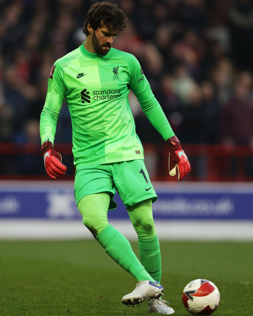 Alisson Becker in bright green Liverpool kit focused ready to kick ball during intense match action Wallpaper