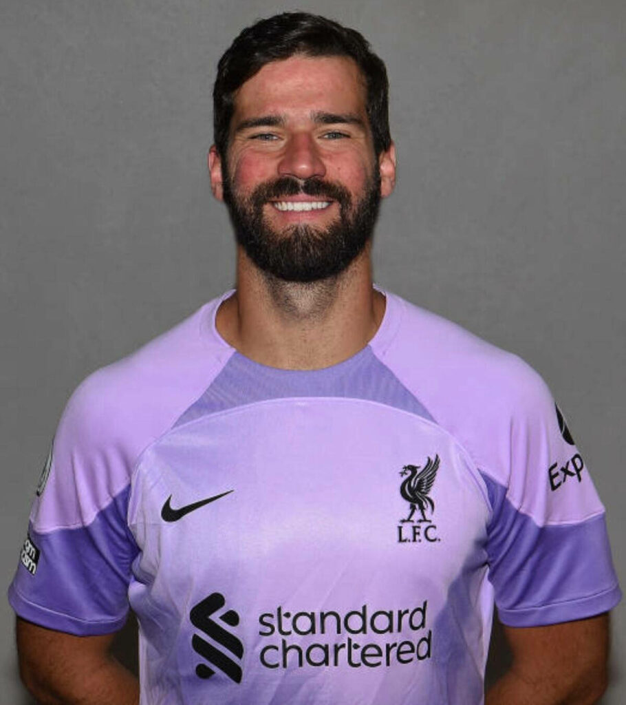 Alisson Becker smiling in Liverpool FC goalkeeper jersey vibrant wallpaper background for fans