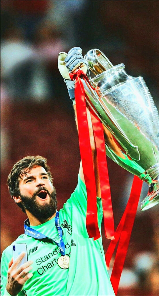 Alisson Becker celebrating football victory holding trophy and wearing medal on field wallpaper
