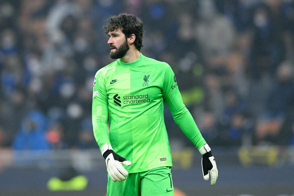 Alisson Becker in neon green Liverpool goalkeeper jersey standing confidently on football pitch Wallpaper
