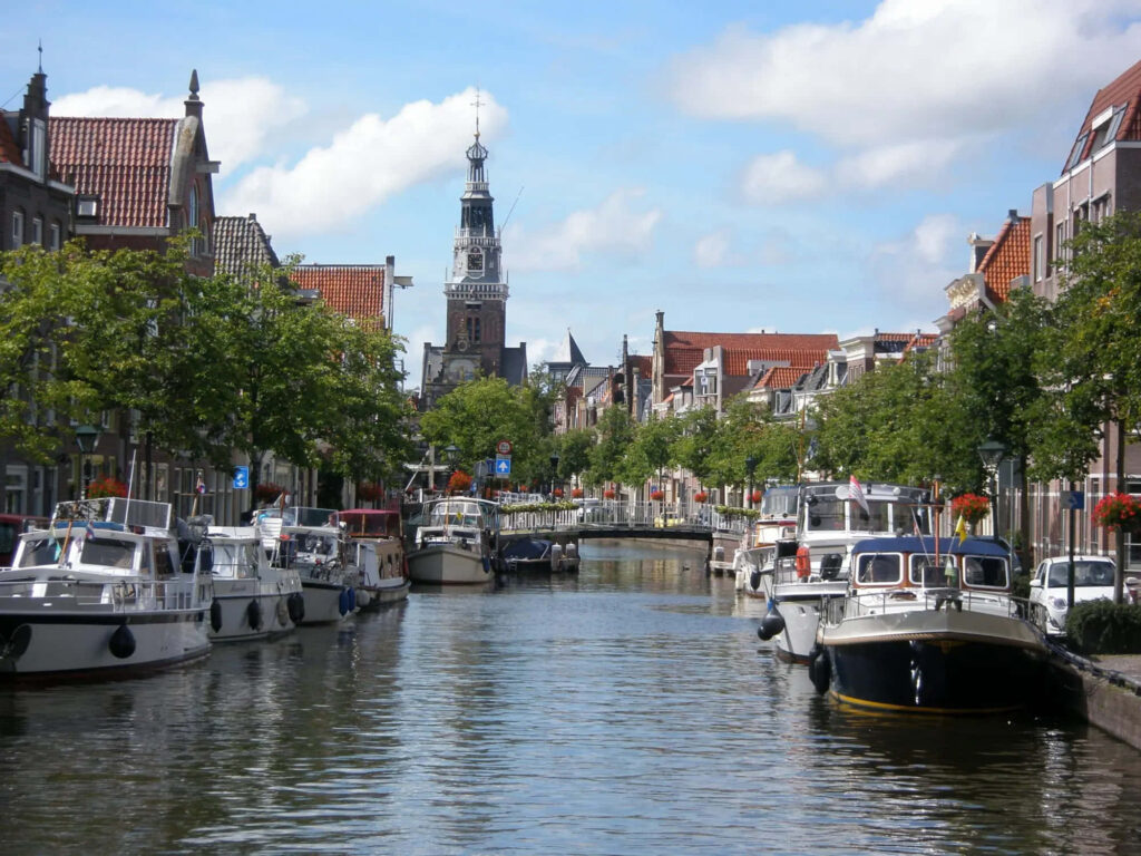 Scenic Alkmaar canal with boats charming buildings and historic tower under bright sky wallpaper