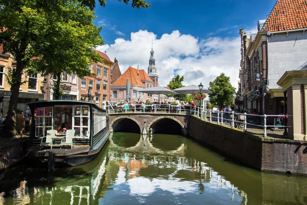 Scenic Alkmaar canal with stone bridge historic orange roofs and lush greenery under blue sky Wallpaper