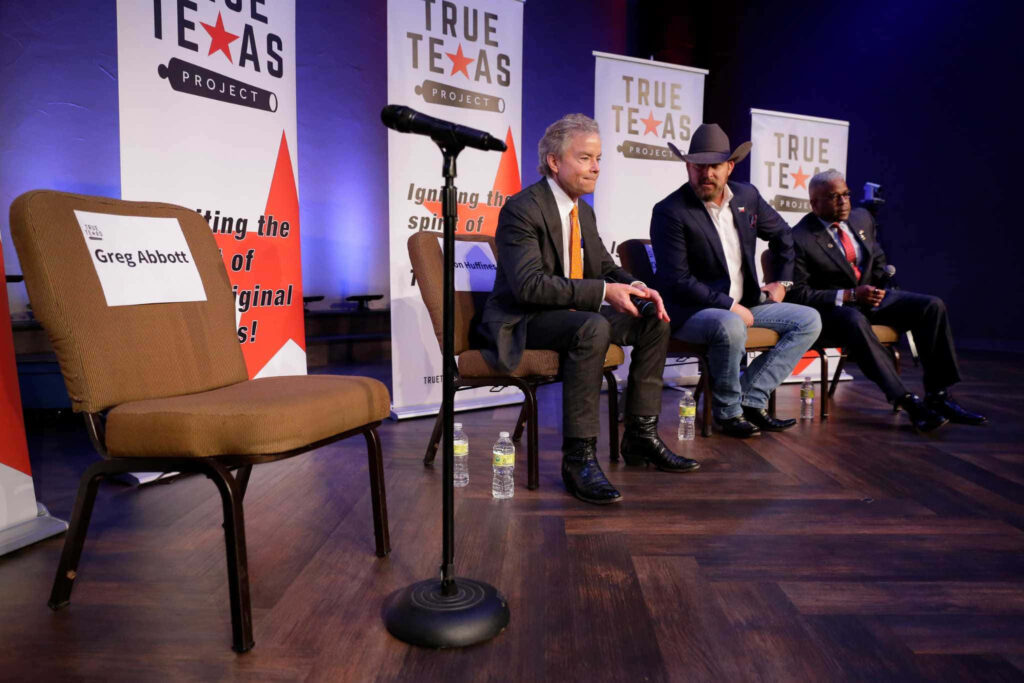 Allen West on stage with panelists at True Texas Project event empty chair labeled Greg Abbott visible Wallpaper