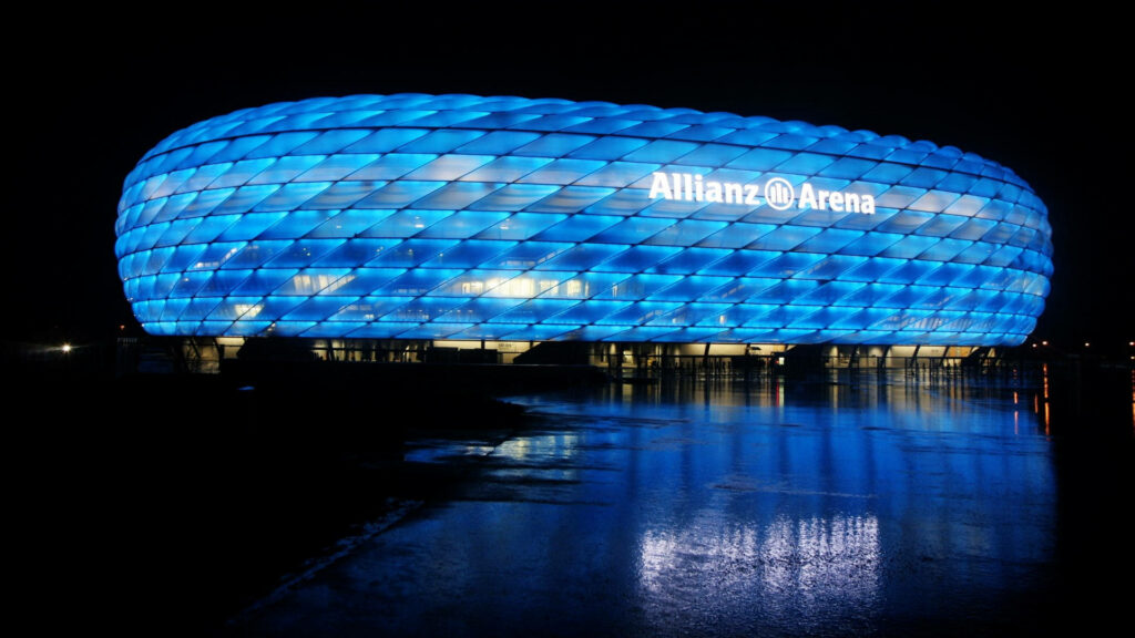 Allianz Arena Munich illuminated blue at night with modern architecture reflected on wet ground Wallpaper