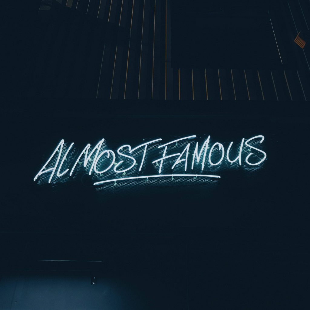 Almost Famous neon sign wallpaper with glowing white script on dark textured mesh background