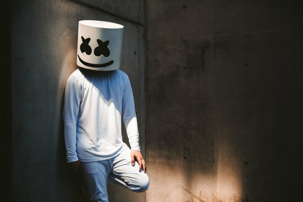 Marshmello in white helmet and outfit leans on concrete wall with dramatic shadows background Wallpaper