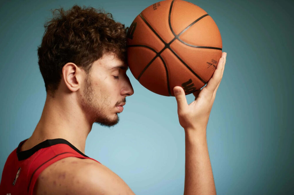 Alperen Şengün peacefully holding basketball against forehead in a focused introspective pose Wallpaper