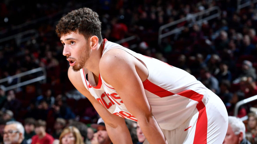 Alperen Şengün focused on basketball court wearing white red uniform in lively arena game Wallpaper