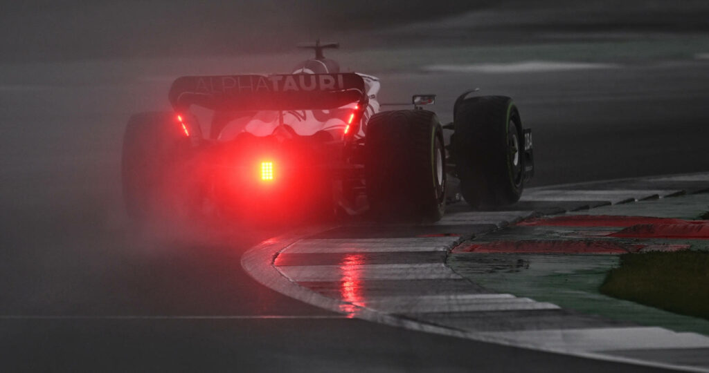 AlphaTauri Formula 1 car racing on wet misty track with glowing rear lights reflection wallpaper