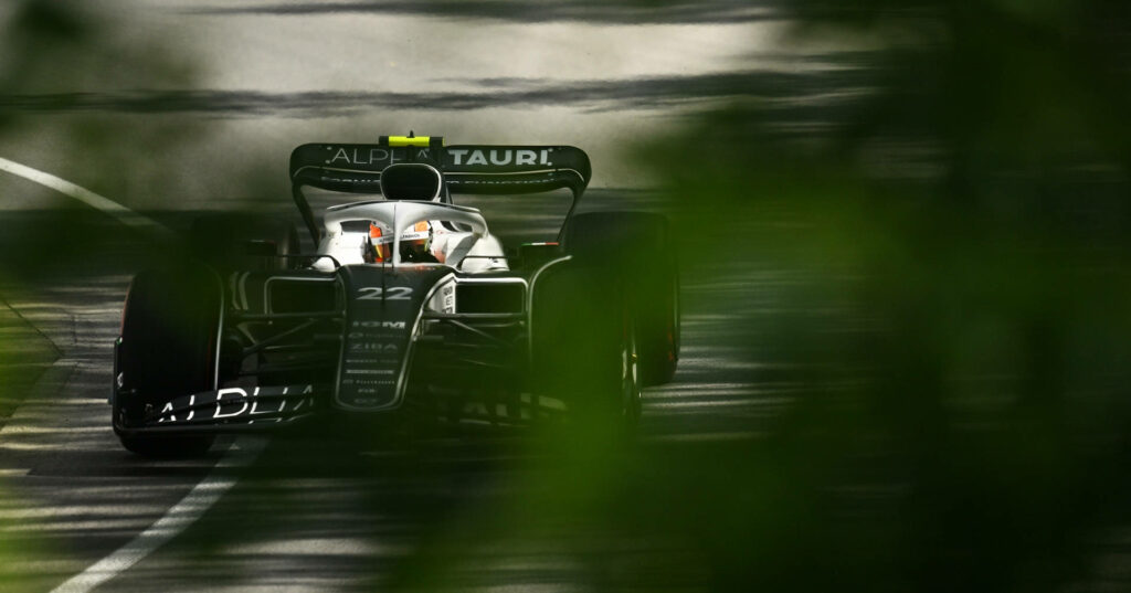 AlphaTauri Formula 1 racecar speeds on track behind blurred green leaves dynamic racing wallpaper