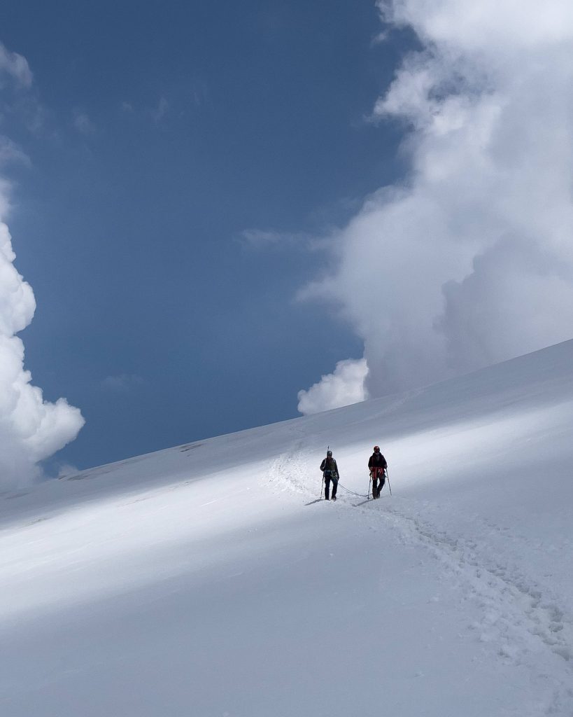Two mountaineers climbing snowy alpine slope under blue sky with fluffy clouds wallpaper