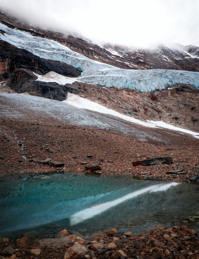 Alpine mountain slope with rocky terrain snow patches and reflective glacier pool wallpaper background
