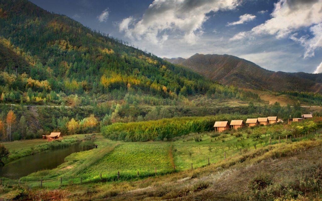 Altai mountains autumn wallpaper with golden forests wooden lodges pond and cloudy sky reflection