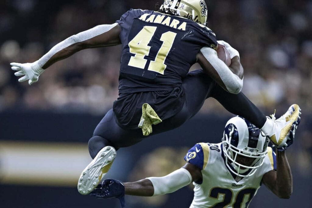 Alvin Kamara leaps over defender during dynamic football play showcasing athleticism and determination Wallpaper