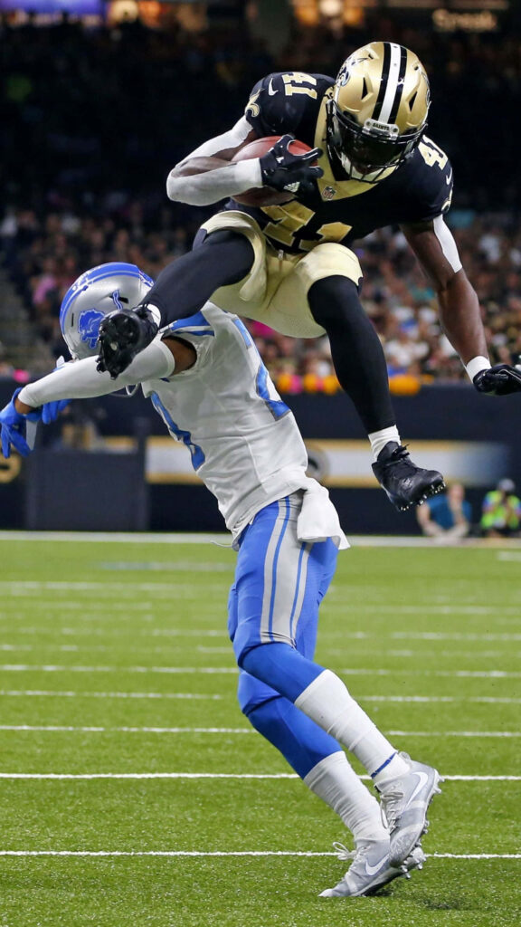 Alvin Kamara leaps over Detroit Lions defender showcasing athleticism in NFL game action wallpaper