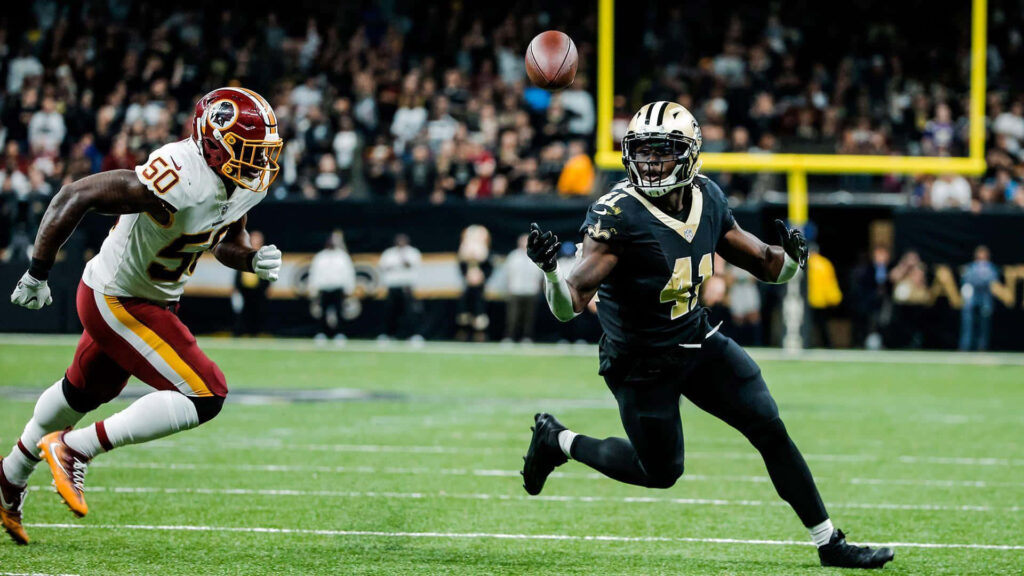 Alvin Kamara sprinting with intense focus chasing football in thrilling NFL game action wallpaper