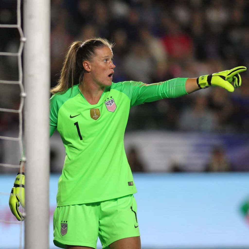 Alyssa Naeher in neon green goalkeeper kit directing defense during intense soccer match wallpaper