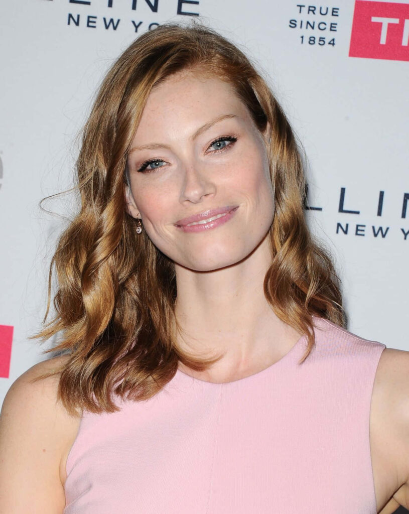 Alyssa Sutherland in soft pink dress posing elegantly at event with branded wallpaper background