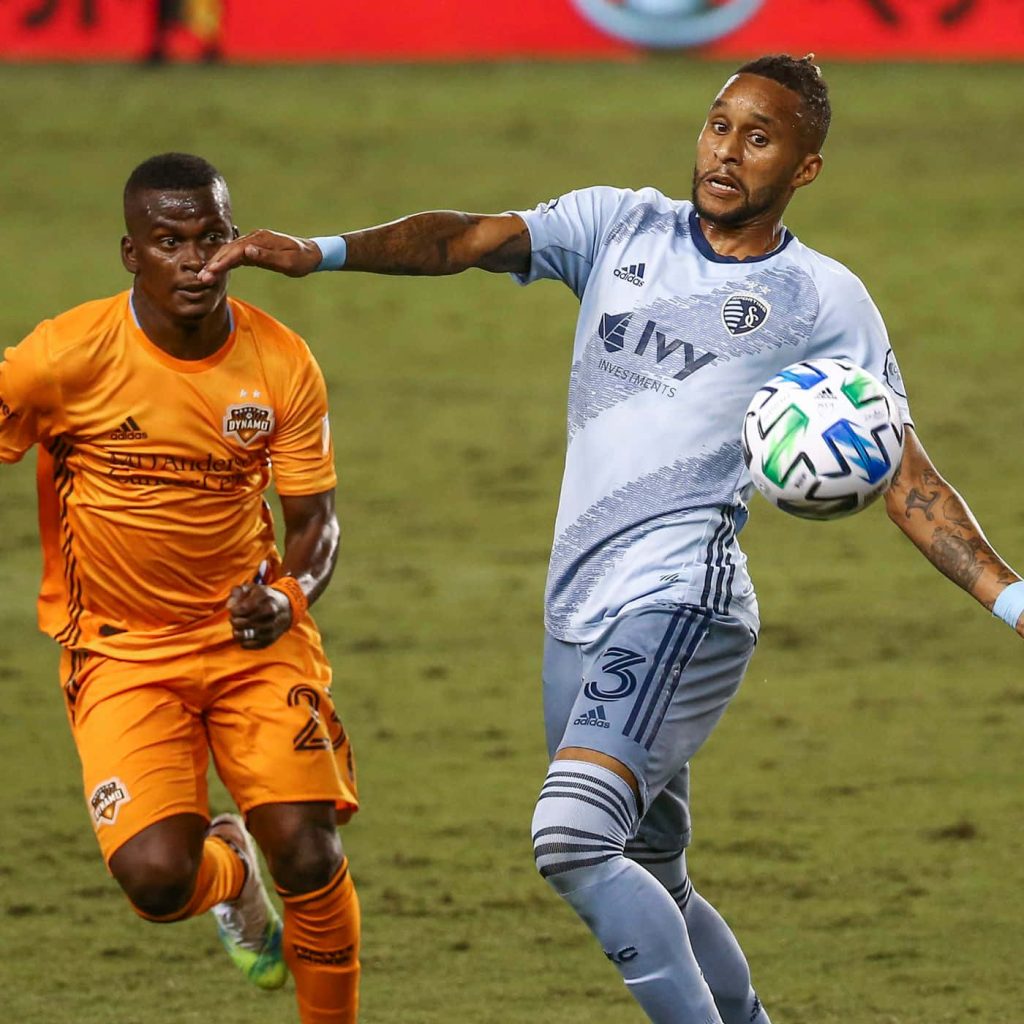 Amadou Dia in light blue Sporting Kansas City kit competing vs Houston Dynamo on grass pitch Wallpaper