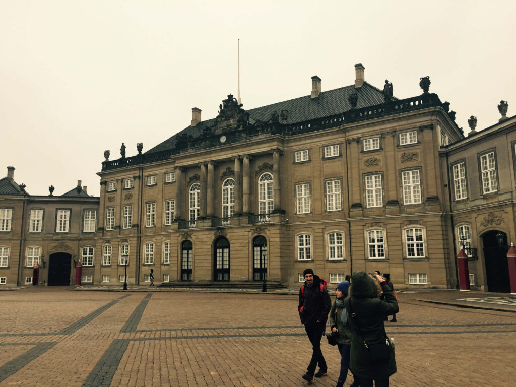 People walking across cobblestone courtyard in front of historic Amalienborg Palace under overcast sky Wallpaper
