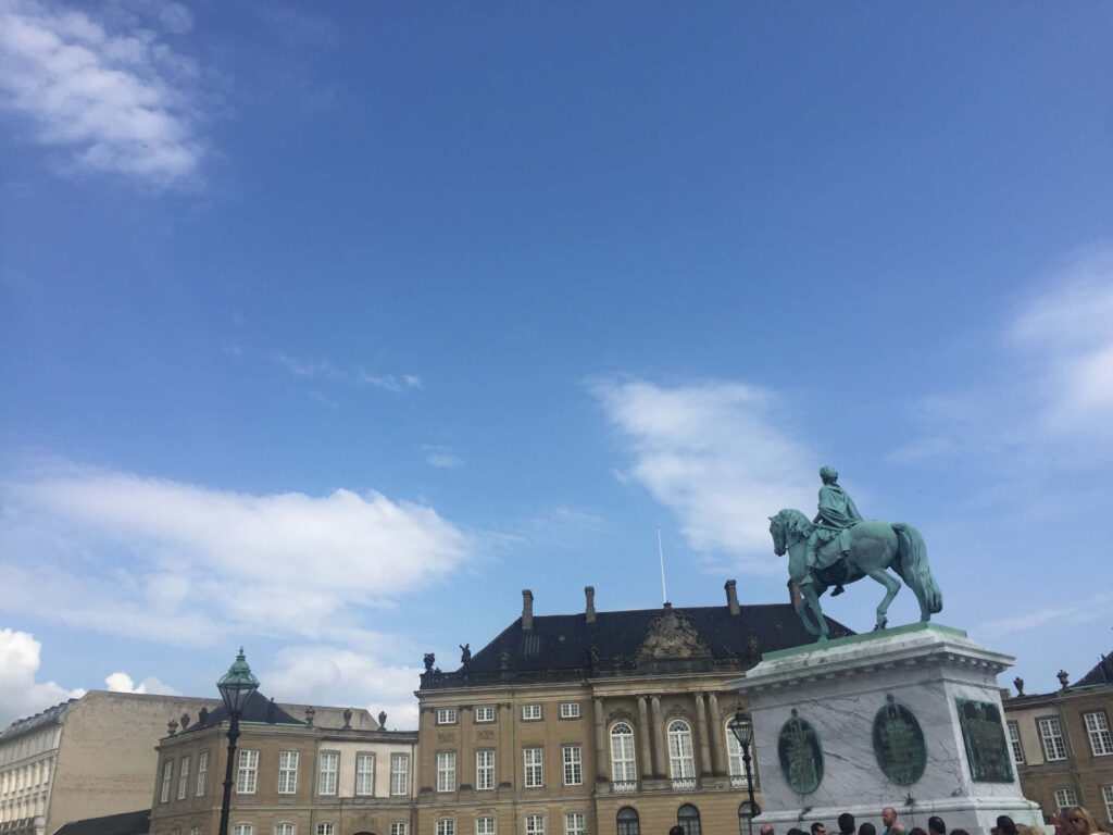 Ground-level view of Amalienborg Palace with iconic equestrian statue and clear blue sky background Wallpaper