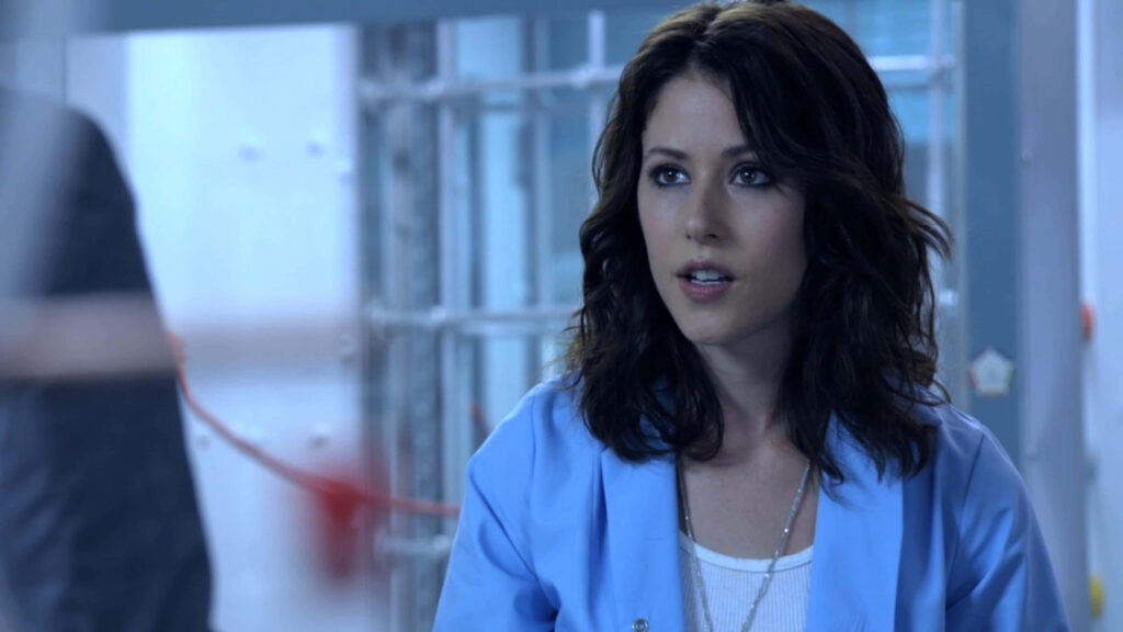 Amanda Crew wearing blue blazer with concerned expression against softly lit wallpaper background