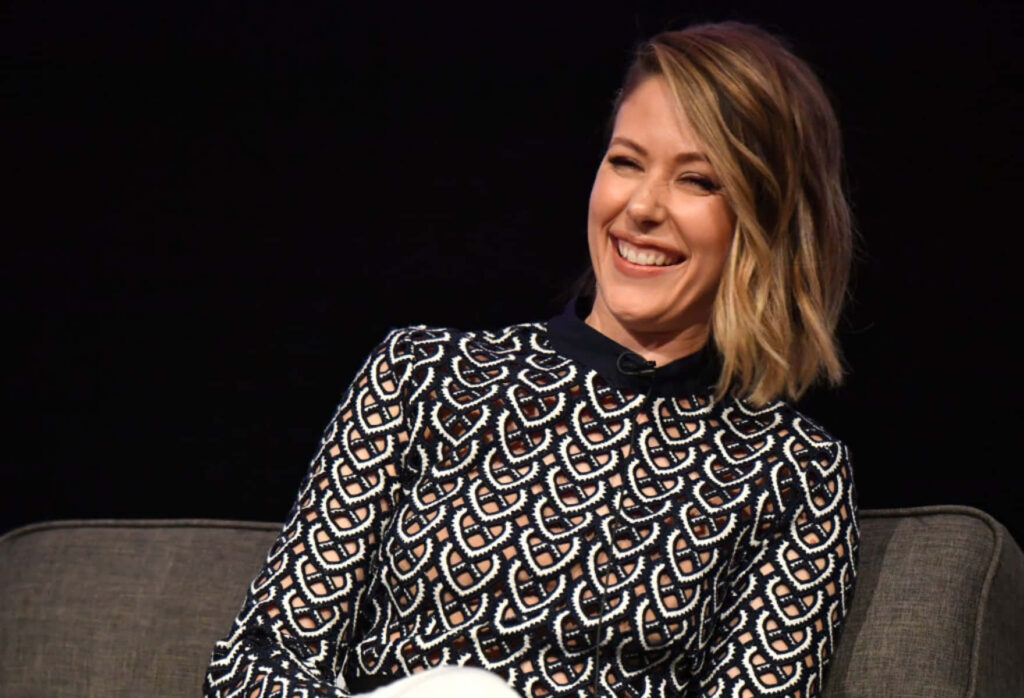 Amanda Crew smiling in patterned top seated on dark sofa during lively panel discussion Wallpaper