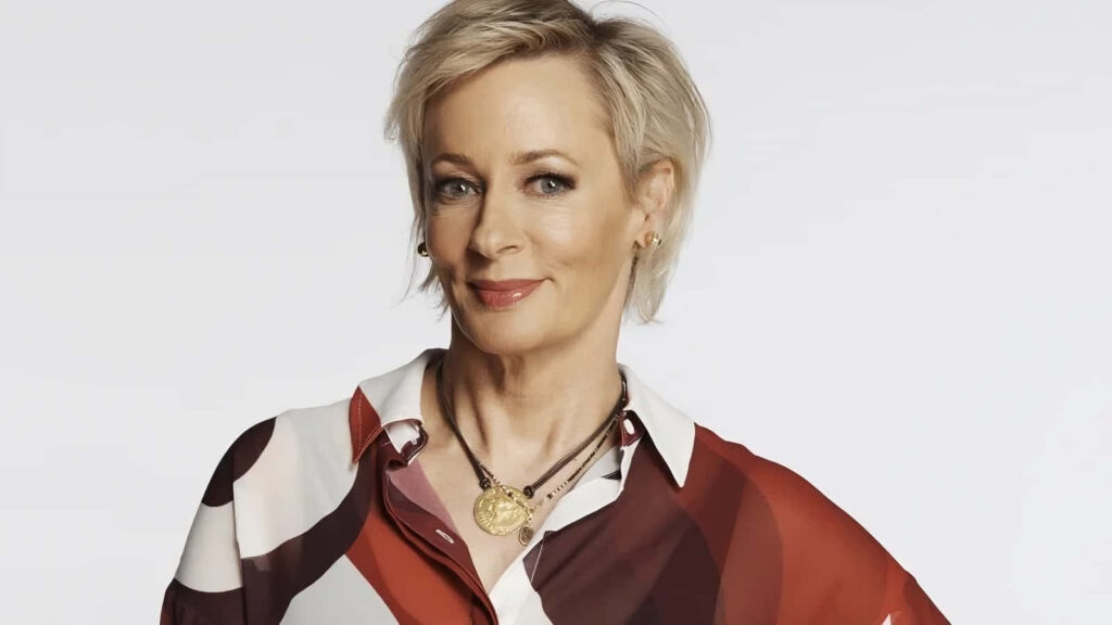Amanda Keller in stylish patterned blouse posing confidently with light wallpaper background