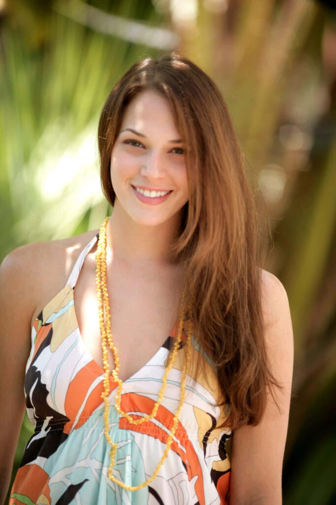 Amanda Righetti smiling in colorful patterned dress and yellow necklace vibrant outdoor wallpaper background