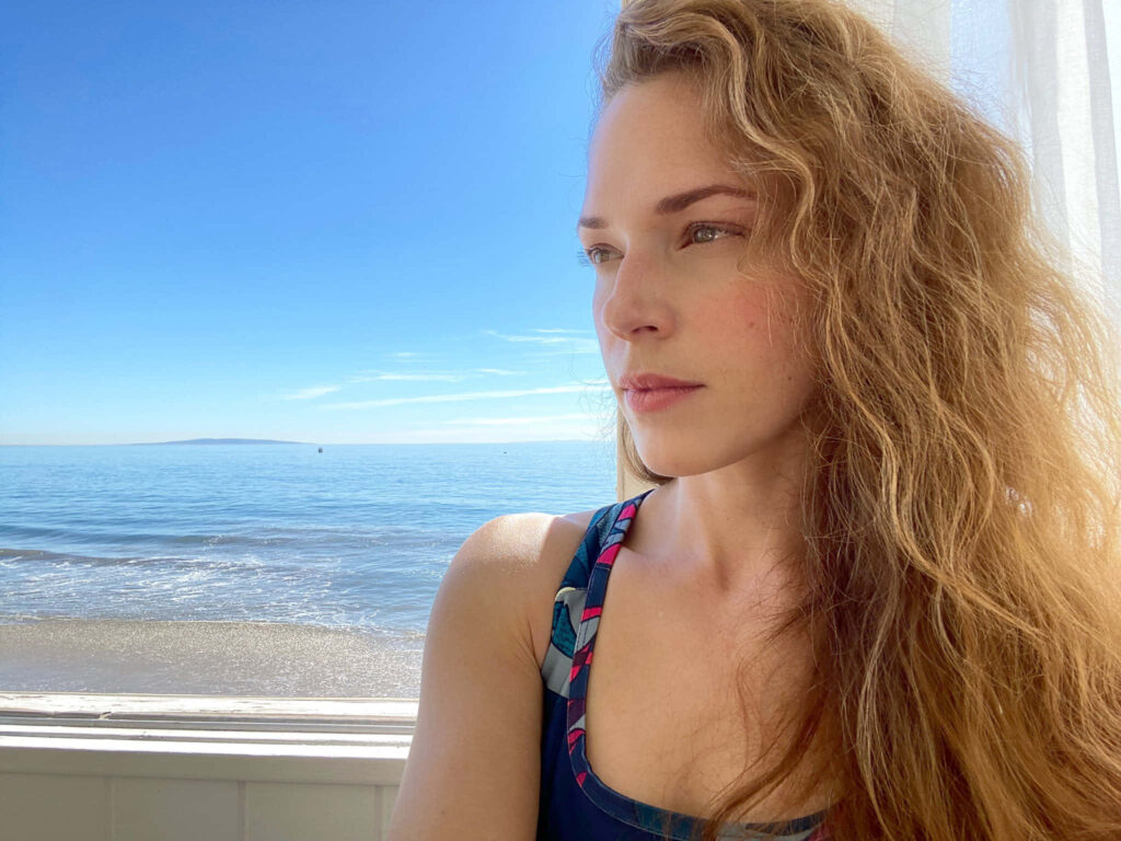 Amanda Righetti contemplative by calm seaside under clear blue sky and soft natural sunlight Wallpaper