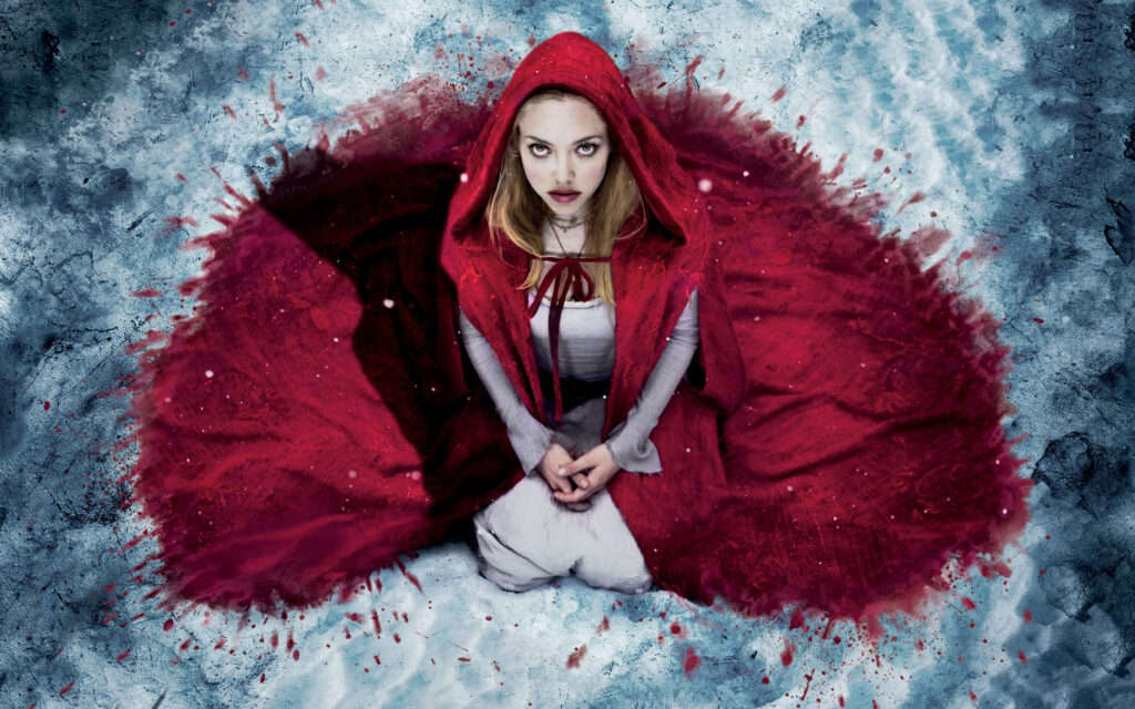 Amanda Seyfried as Red Riding Hood in a red cloak sitting in snowy forest wallpaper background