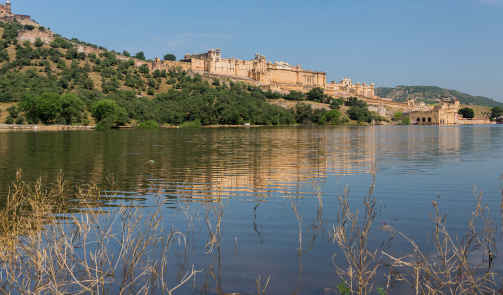 Amber Fort reflected in calm lake waters surrounded by lush hills under clear blue sky wallpaper