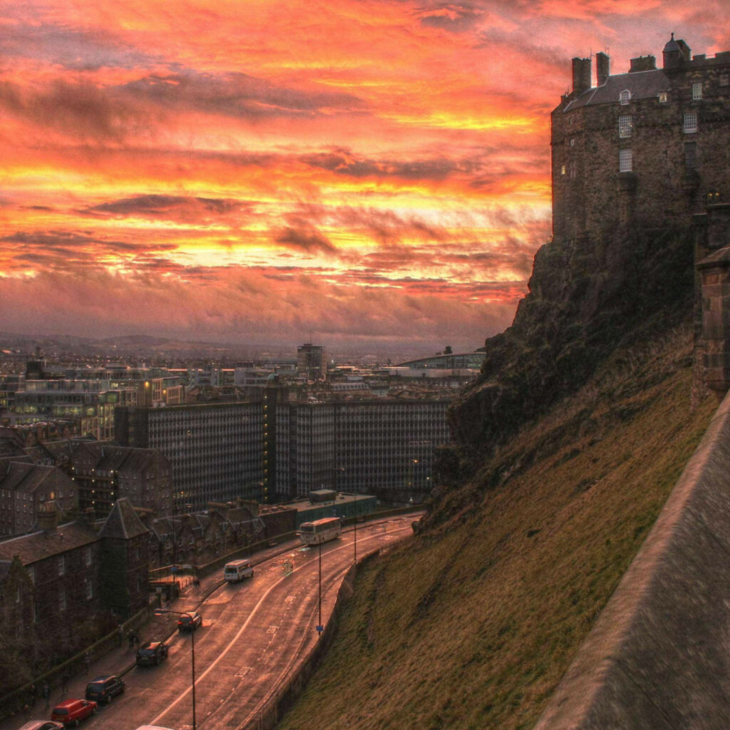 Edinburgh Castle at sunset with amber sky overlooking city roads and modern buildings background Wallpaper