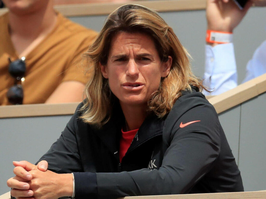Amélie Mauresmo seated in crowd focused watching event with wallpaper background visible
