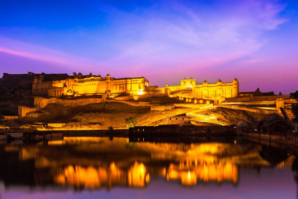 Amer Fort illuminated at dusk with golden lights reflecting in calm waters and vibrant sky Wallpaper