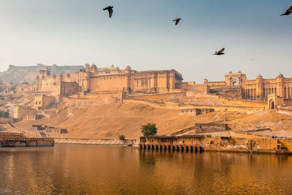 Amer Fort majestic architecture reflected in calm water with birds soaring in clear sky wallpaper