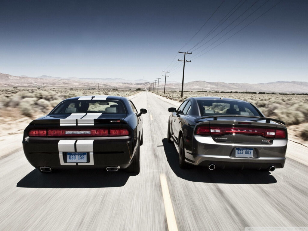 Two American muscle cars drive side by side on desert highway showcasing bold design and power Wallpaper